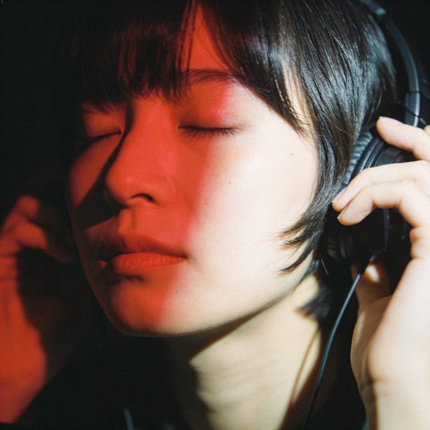 A listener in headphones, eyes closed, in red light